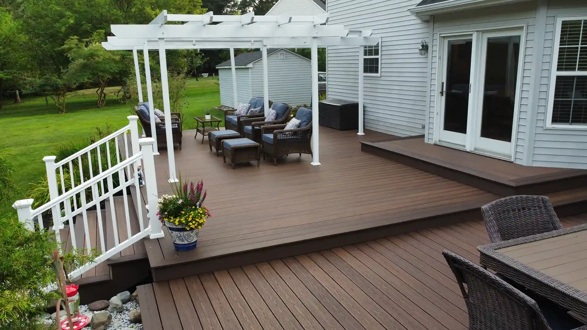 screened porch vs deck Photo of a large, brown composite deck attached to a light-colored house, featuring a white pergola and outdoor furniture.